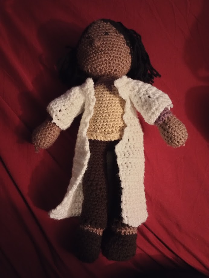 The same doll, slightly in shadow, wearing a long white crocheted lab coat over his other clothes