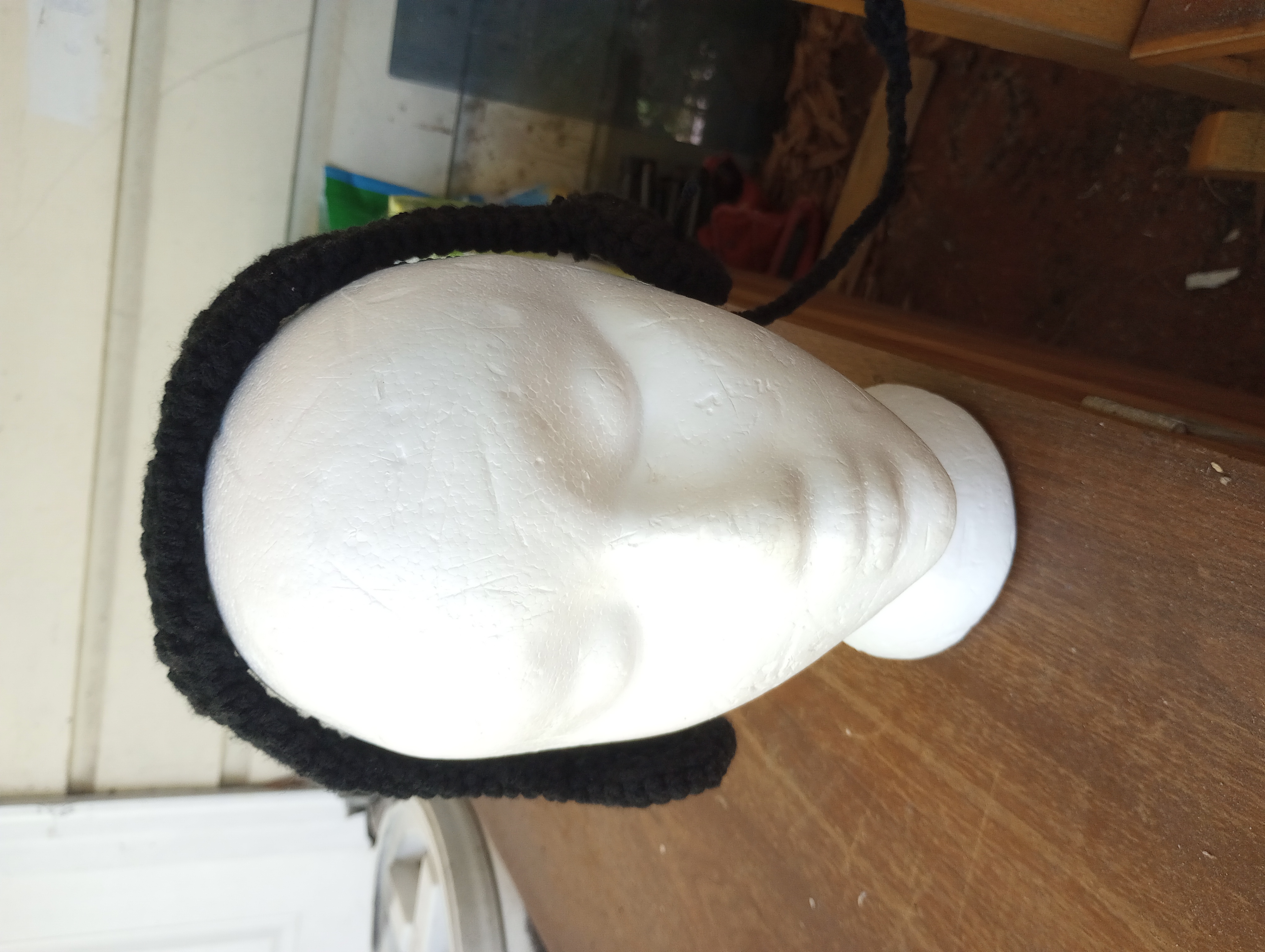 A close-up of the white styrofoam head sporting a pair of crocheted black headphones