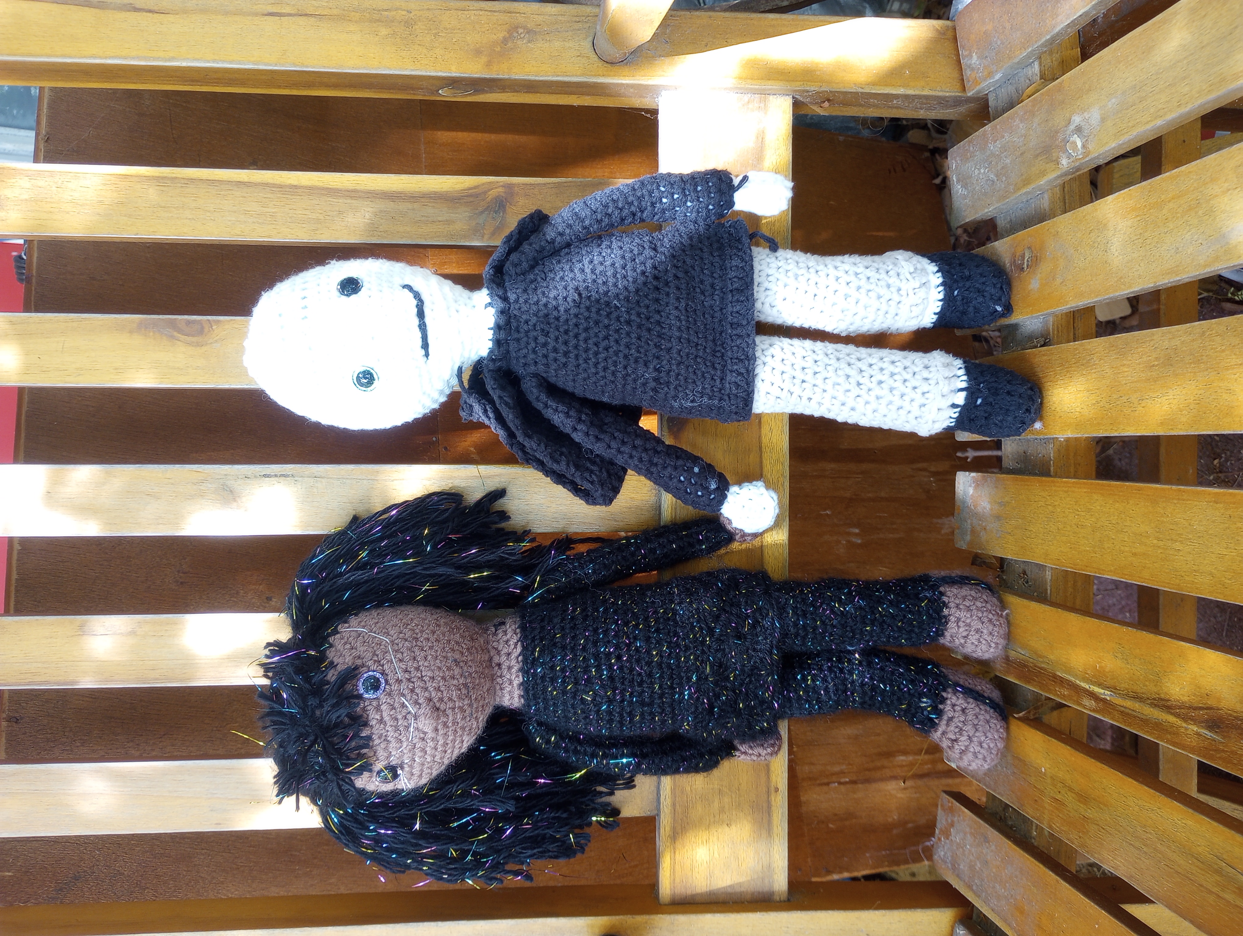 A picture of the doll seeming to hold hands with another doll, a skinny girl in a black tunic and trousers crossed with filaments, black hair with more filaments running through them, and wires connecting to her eyes