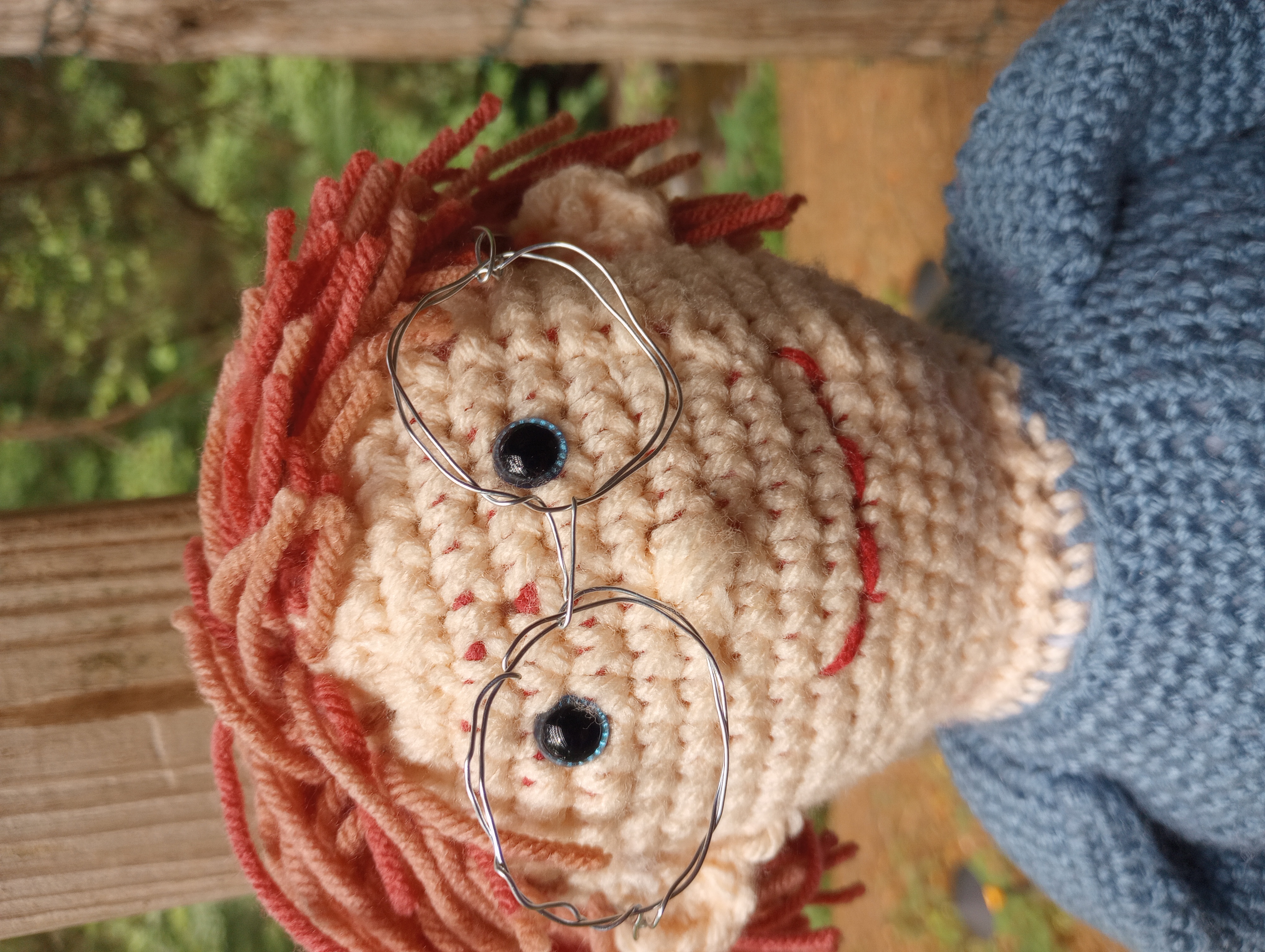 A close-up of the doll's face, displaying the glasses and stitched smile.