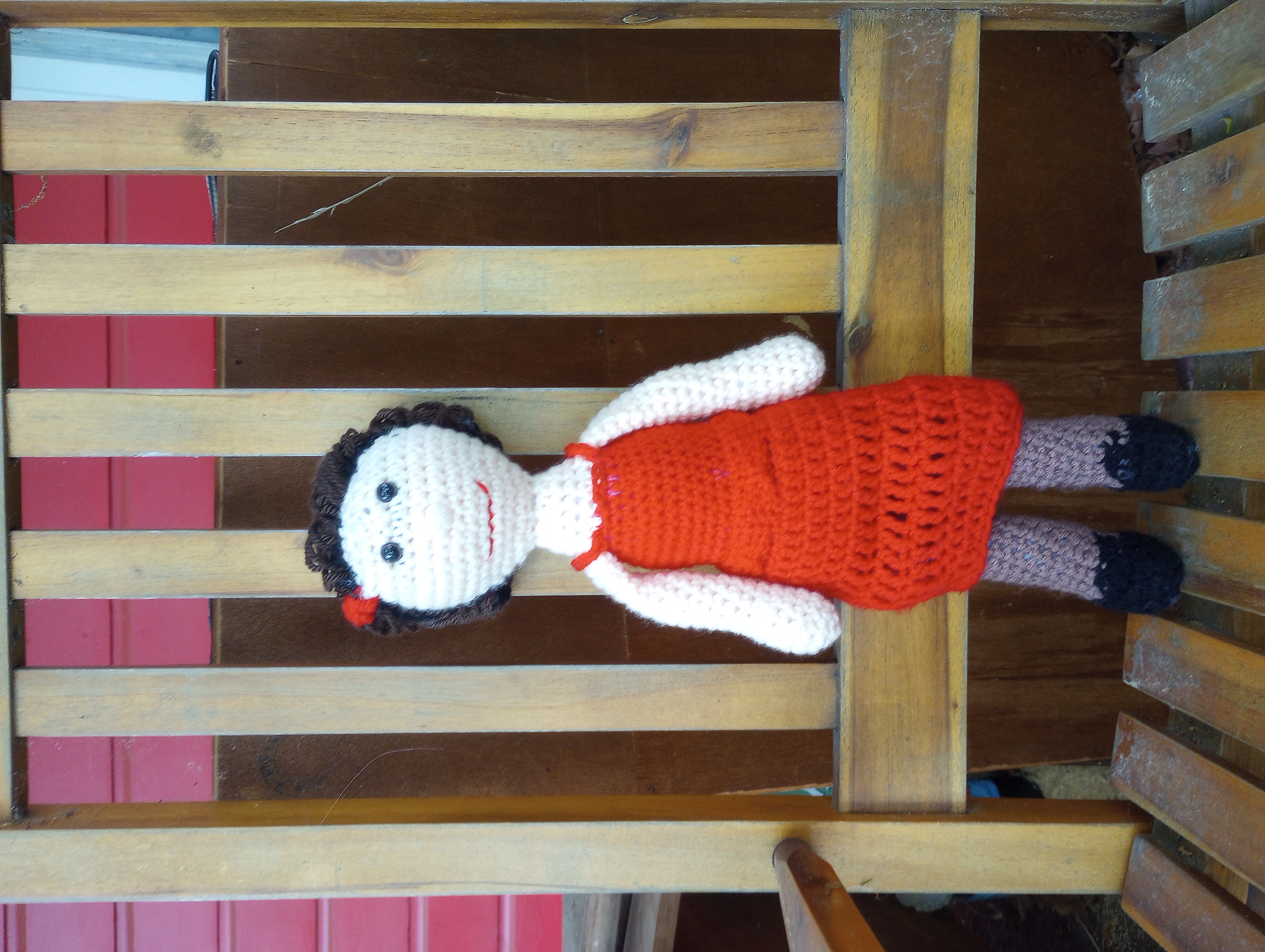 A crocheted doll with pale skin, brown hair swept into an updo and pinned with a red rose, and brown eyes, wearing a red strappy dress, tan pantyhose, and black shoes