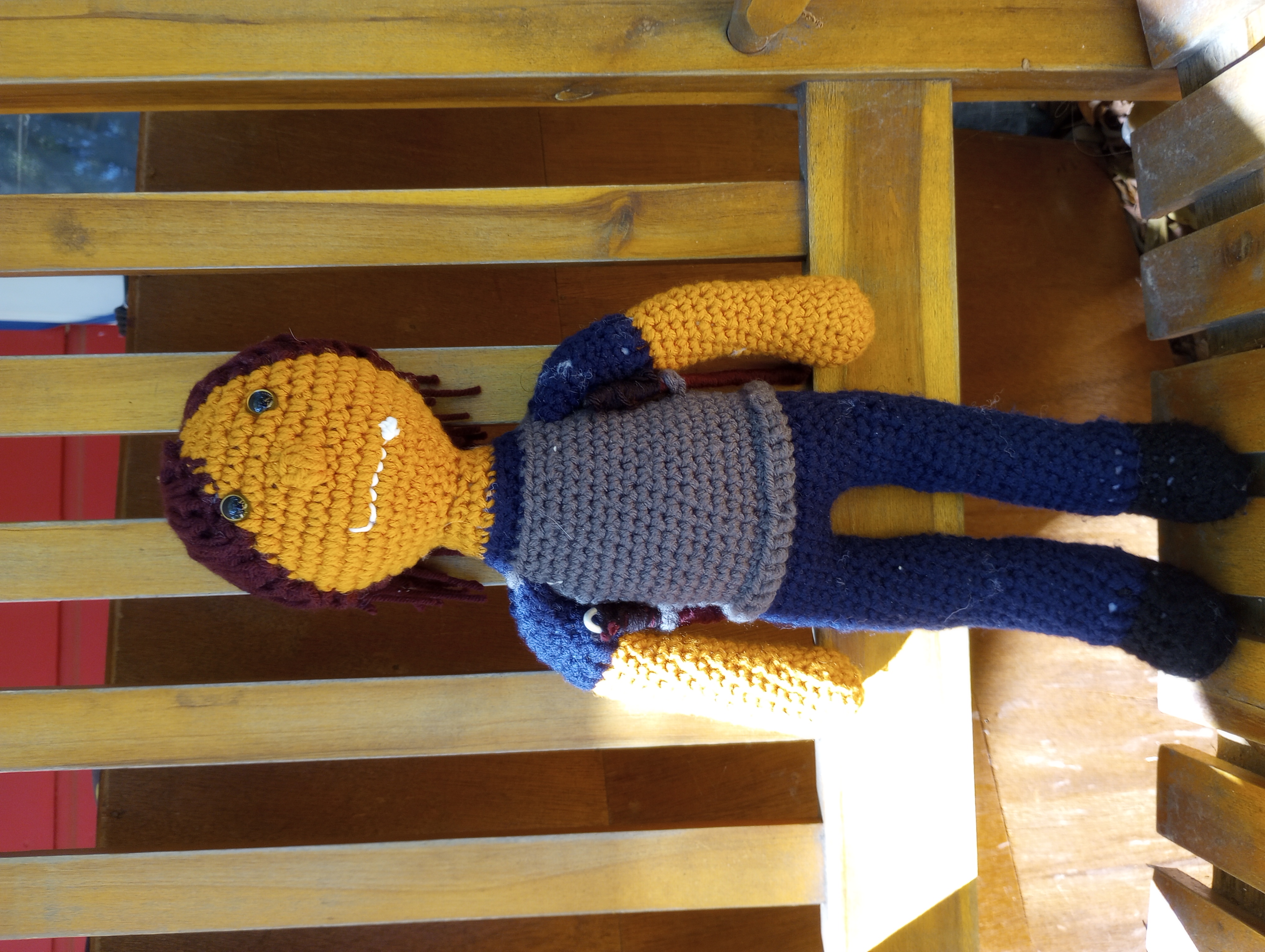 A crocheted doll of Zongroff Gral'Shaak, an orc with orange skin, reddish-brown hair, and yellow eyes, wearing a navy blue shirt and trousers with black shoes and grey armor, with two sticks on either side